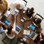 Top view of a diverse team collaborating in an office setting with laptops and tablets, promoting cooperation.